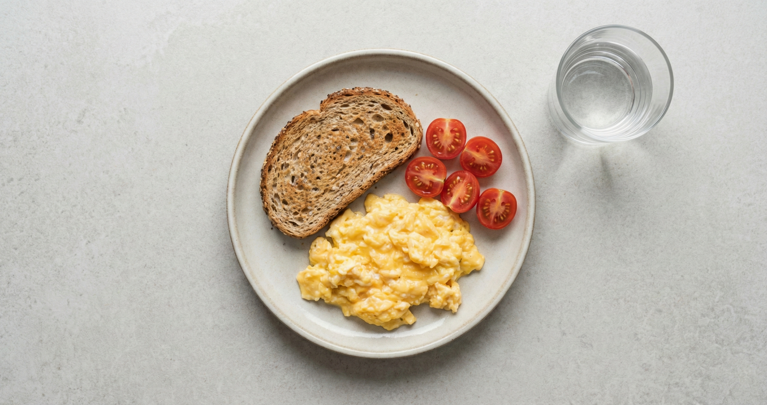 Einfaches Fr&uuml;hst&uuml;ck von oben: R&uuml;hrei, Vollkornbrot, Tomaten, Glas Wasser