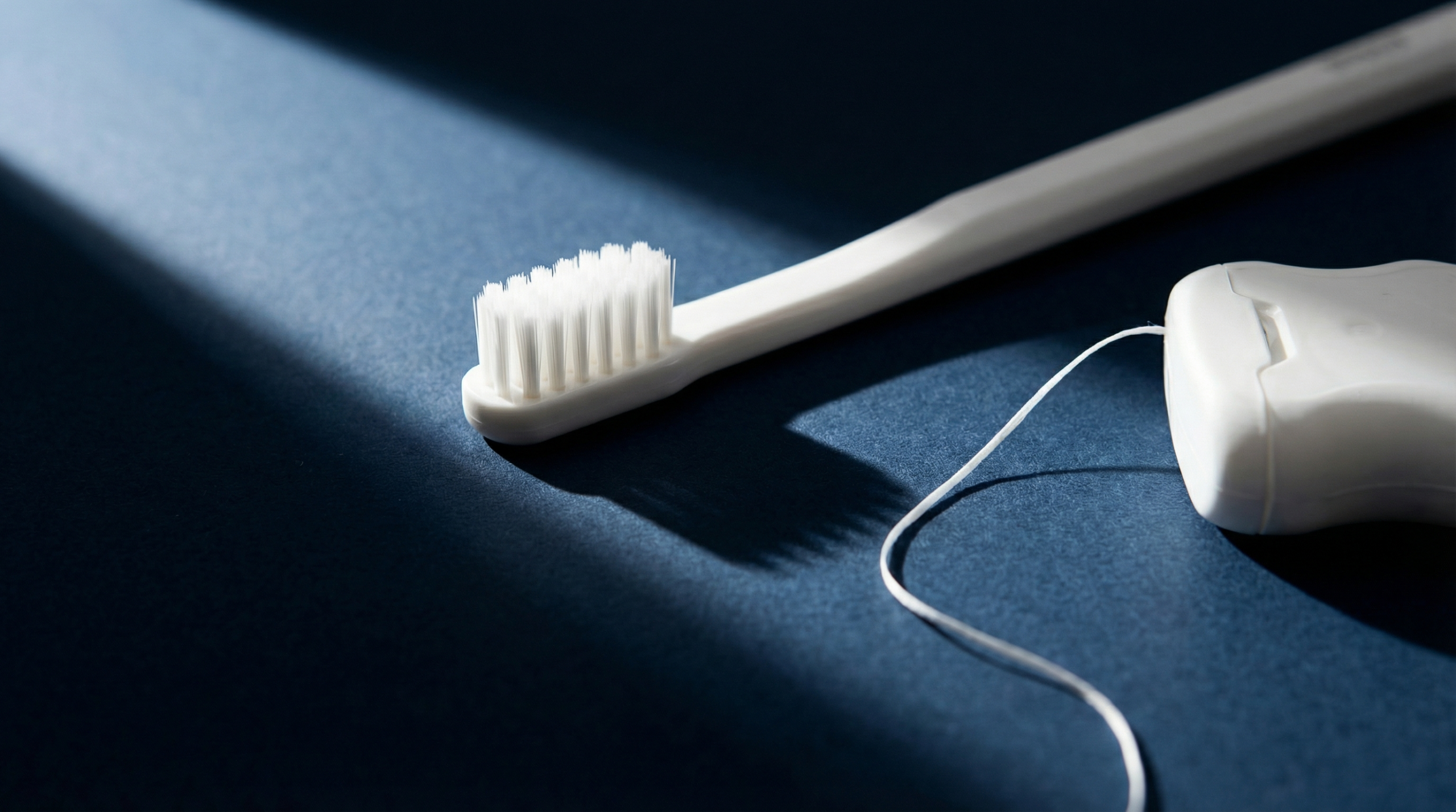Nahaufnahme einer Zahnb&uuml;rste und Zahnseide auf dunklem Hintergrund, minimalistisch